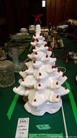 Full view of vintage white ceramic Christmas tree with red bulbs and red star topper, placed on green table with other antique collectibles around.