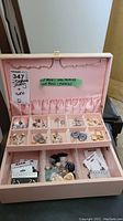 Photo of pink jewelry box with multiple compartments holding various pairs of earrings, ring holders, and elastic pockets