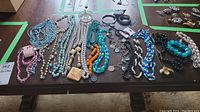 Photo showing a large assortment of costume jewelry including various beaded necklaces and bracelets as well as a ring dish on a wooden table.