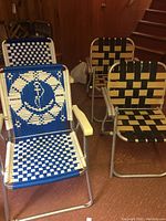 Four vintage lawn chairs in a basement setting. Two blue and white nautical design chairs and two black and tan woven pattern chairs visible.