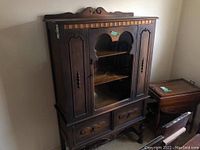 Front view of the wood hutch showing glass door with carved wooden framing, two drawers below, decorative top, and carved legs.