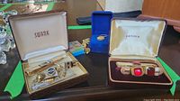 Overview photo showing multiple men's jewelry items including Swank tie clip and cufflinks set, Eaton's set with red glass, and blue enamel lapel pin.