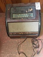 Front and top view of a vintage Philco wood case radio with a glass tuning dial showing AM frequencies and a fabric speaker grill. Shows signs of wear and age including scratches and paint loss.