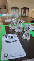 Overview of three Swarovski crystal bears of different sizes on a table with auction tag. Smallest bear missing an ear.
