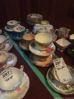 Full view of the six teacups and saucers arranged on table showing various floral and gold accent designs