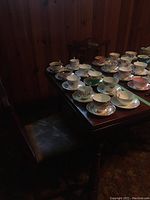 Wide view showing ten tea cups and saucers arranged on wooden table
