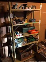 Full view of the metal utility shelf loaded with various small figurines, brushes, tools, and containers.