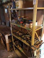 Metal utility shelf with several shelves containing various tools and cans, showing sturdy steel construction with cross-bracing.