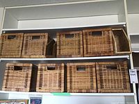 Overview of eight square wicker storage baskets with cutout handles and two wicker magazine holders arranged on shelves.