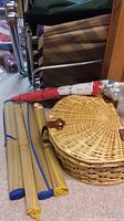 Shows round woven picnic basket, three rolled mats with blue and yellow ties, and one umbrella in plastic wrapping