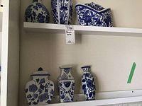 Wider view showing one larger curved blue and white porcelain piece with floral design along with the three smaller pieces on the shelf.