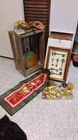 The overall assortment including the tapestry laid flat, framed keys leaning against a door, wooden box with pumpkin painting, two colorful masquerade masks on top, and various shiny gold heart ornaments placed on the floor.