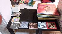 Photo showing a table with stacked vinyl albums and displayed CDs including The Beatles and Buddy Holly.