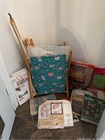 Overall view of the craft bag filled with embroidery frames and needlepoint stitchery kits with brand packaging visible.