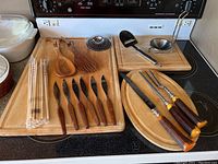 Photo showing wooden cutting boards, salad servers, chopsticks, steak knives and carving set with forks and knives.