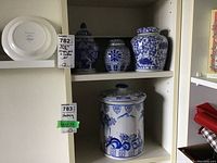 Full view of all four jars on a white shelf, three ginger jars and one taller cookie/pickle jar with lids, displaying blue and white ceramic patterns.