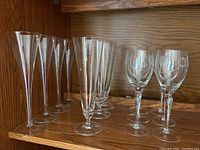 Photo showing 4 clear champagne flutes, 3 parfait glasses, and 2 etched wine glasses on wooden shelf.