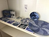Photo showing two Delft blue decorative plates, several rectangular Holland Cruise Line ceramic tiles, and two clear shot glasses.