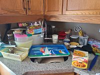 Full view of kitchen countertop with various kitchenware items including storage containers, jars, trays, and wraps.