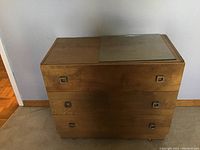 Front view of light brown Mid-Century Modern dresser with three drawers and glass inset top panel, showing overall condition and drawer pull detail.