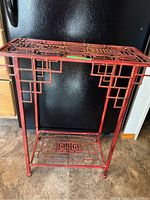 Front view of the red metal table showing Asian motif lattice design