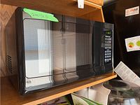 Front and top view of Hamilton Beach black microwave, showing approximate dimensions taped on top (20x14x12). Exterior shows minor wear, reflective surface visible.