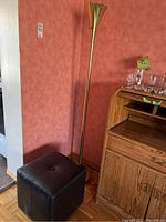 Photo of black cube PVC leather ottoman and tall brass torchiere lamp beside a wooden roll-top desk, showing size and condition of both items.