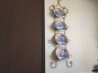 Full view of the metal wall rack holding four decorative plates vertically on a wall with a door nearby.