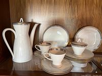 Wide view of Rosenthal coffee pot, 2 cups, 3 saucers, sugar bowl with lid, and 6 cake plates with gold accents on white porcelain.