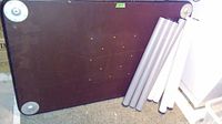 Wooden table top placed on floor with two sets of four detached cylindrical legs leaning against it.