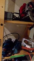 Wide shot of wooden shelves with various power tools including circular saw, two blue grinders, and a jigsaw on bottom shelf.
