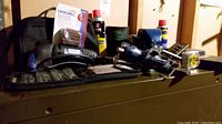 Tools and parts seen on top of a filing cabinet including a blue bench vice, Dremel contour sander, screwdriver bit set, WD-40 can, and assorted small tools.