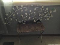 Photo of decorative metal wall art mounted above a folding TV tray, showing details of the leaf design and overall size