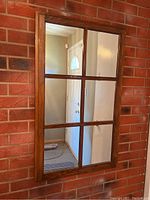 Front view of rectangular wood framed mirror with six-pane window style design reflecting an interior doorway and hallway.
