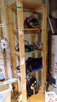 Wooden shelving unit in basement partially loaded with tools and equipment (not included). Straight front view showing four tiers of shelves made from unfinished wood boards.