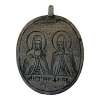 Close-up of amulet front showing two saints with halos and Cyrillic inscription below.