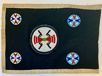 Full view of black wool backing with beige border and five beaded spheres arranged with one large central and four smaller circles.