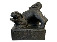 Side view of dark ceramic Foo Dog sculpture on a decorative base showing detailed mane and curled tail.