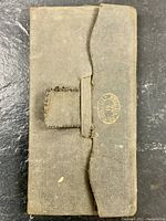 Front cover of small brown cloth-bound journal with flap and clasp closure. Worn and aged cloth with an embossed stamp.