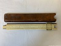 Slide rule with leather case, laid flat showing full length and condition of both items.