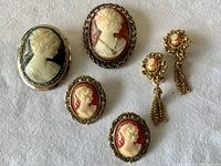 Five vintage cameo jewelry pieces displayed on white background showing front and profile female carvings.