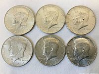 Six 1964 Kennedy half dollar coins front side showing JFK profile and year.