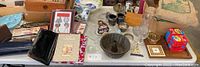Overview of table with purses, framed cards, glassware, wooden box, and collectible items