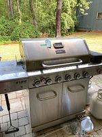 Front view of the Nexgrill large stainless steel gas BBQ showing six burner knobs, built-in thermometer on the hood, and double-door cabinet below.