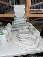 Complete stacked view of the porcelain dinner set featuring plates, square bowls, cups, platters, and Corningware dishes with lid.