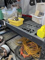 Photo showing yellow container with metal locksets, stacked plastic storage bins, and coiled extension cords beneath shelf.