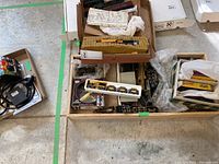 View of a wooden drawer containing multiple boxes with various HO scale train parts, including a foam tray holding a yellow steam engine and other small parts scattered around.