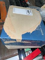 Top view of the original blue cardboard box showing damage, peeling, and tape residue.