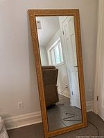 Full length mirror leaning against a wall, showing the overall size and shape, with a gold/yellow carved wooden frame.