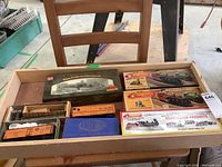 Overview of the lot showing multiple boxed and unboxed model rail cars on a wooden tray on chair.